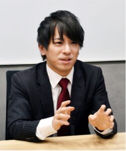 Mr. Toyohito Sawada sitting behind a desk and talking.